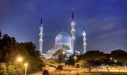 HD desktop wallpaper featuring the illuminated Sultan Salahuddin Abdul Aziz Mosque at dusk, showcasing its iconic blue dome and tall minarets against a twilight sky.