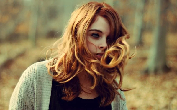 HD desktop wallpaper featuring a beautiful woman with flowing hair, standing in a blurred forest background with soft, autumnal colors.