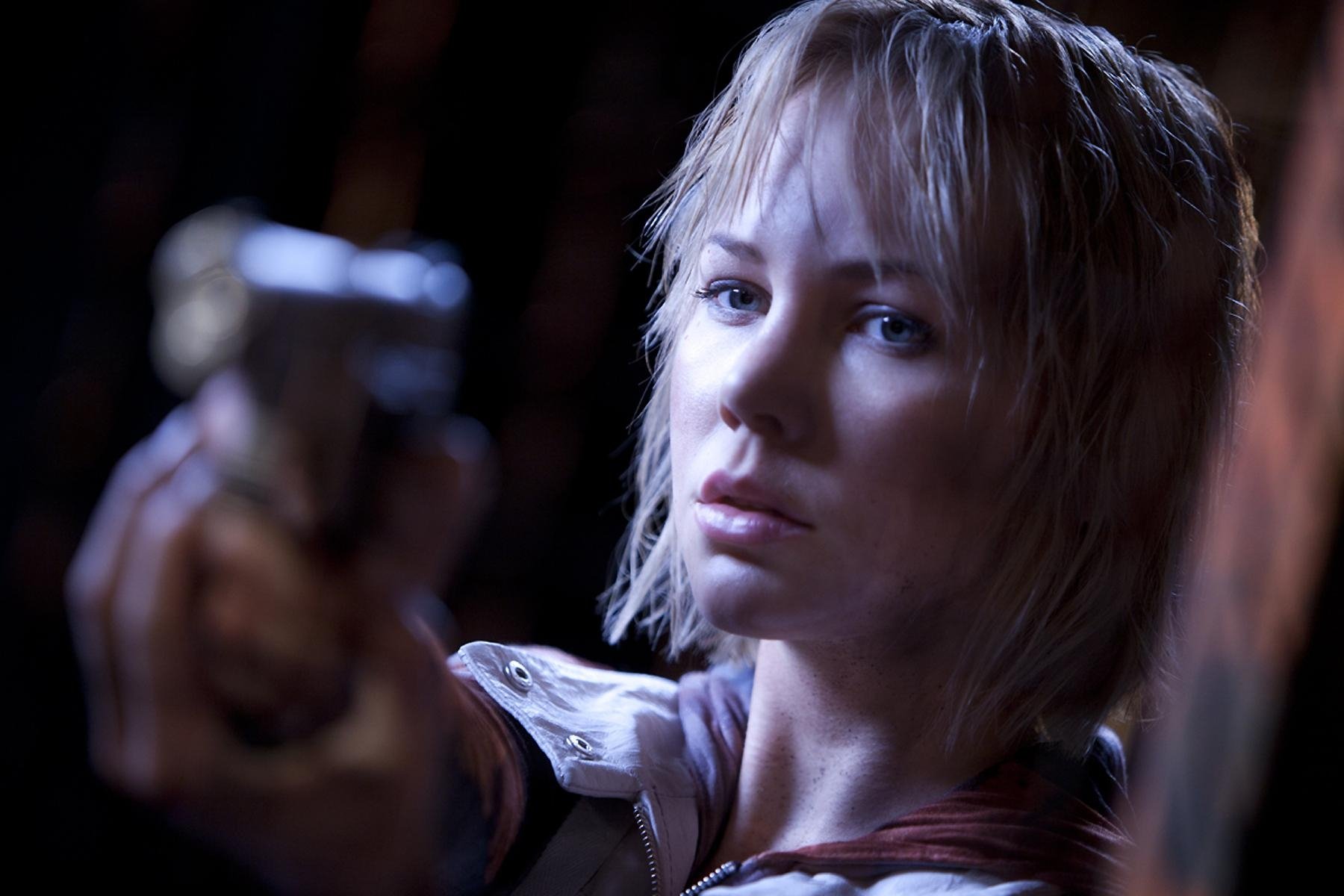 HD PC desktop wallpaper featuring a tense scene from the movie Silent Hill: Revelation with a close-up of a woman aiming a gun in dim lighting.