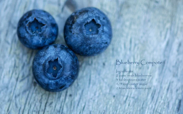 HD PC desktop wallpaper showing a close-up food photo of three blueberries on weathered wood with faint Blueberry Compote recipe text.