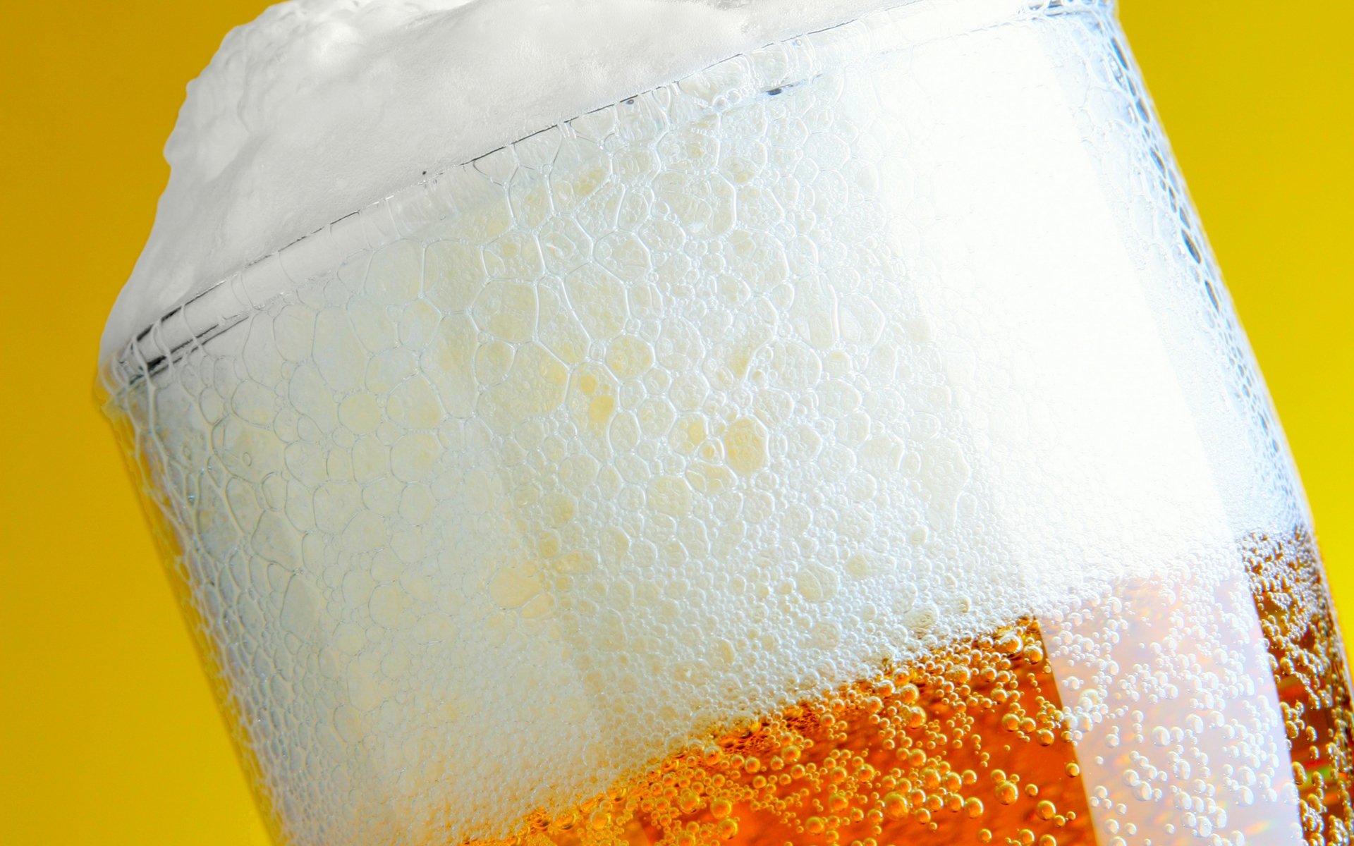 Close-up HD PC desktop wallpaper of a frosty glass of beer with rich amber color and thick foam head, highlighting refreshing bubbles and texture.