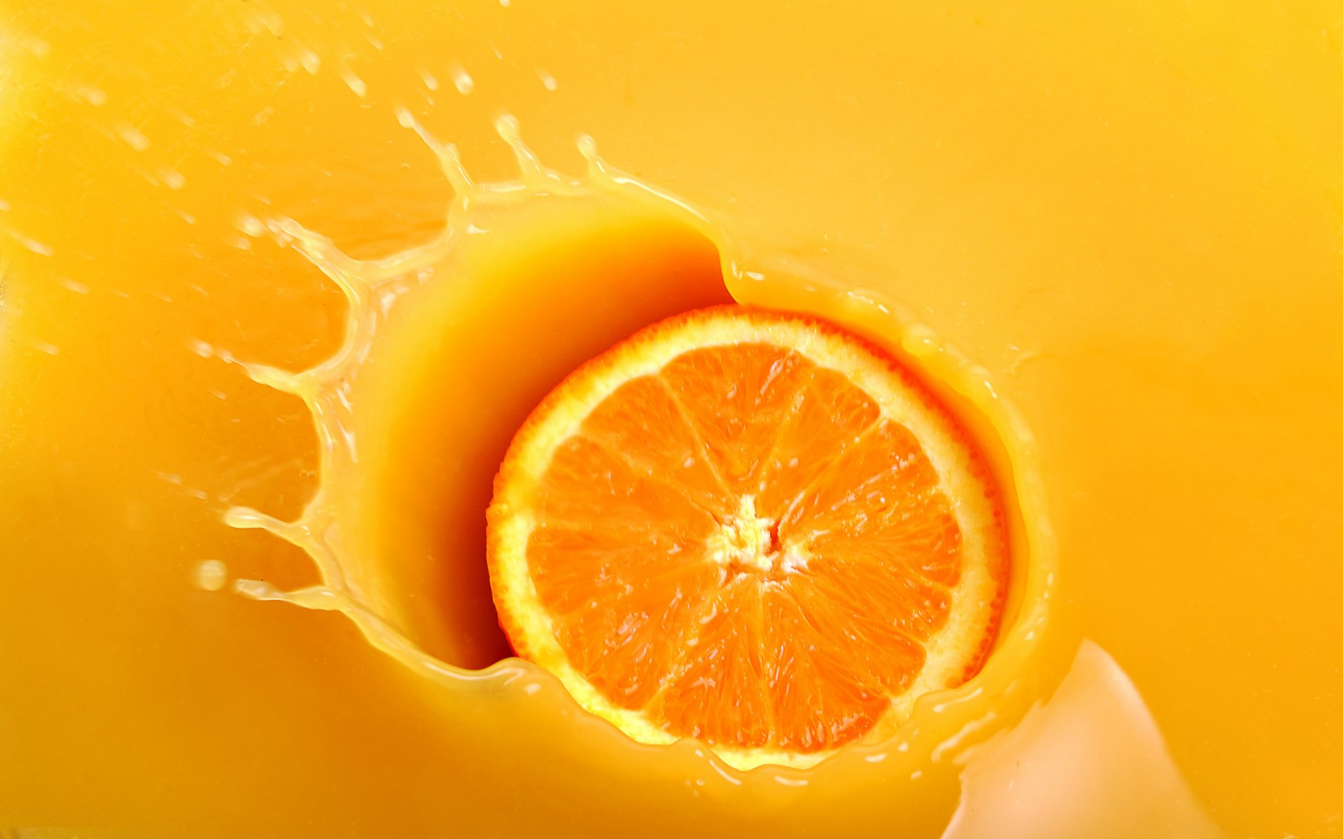 HD desktop wallpaper showing a close-up of an orange slice splashing into vibrant orange juice, highlighting food and the vivid orange color.