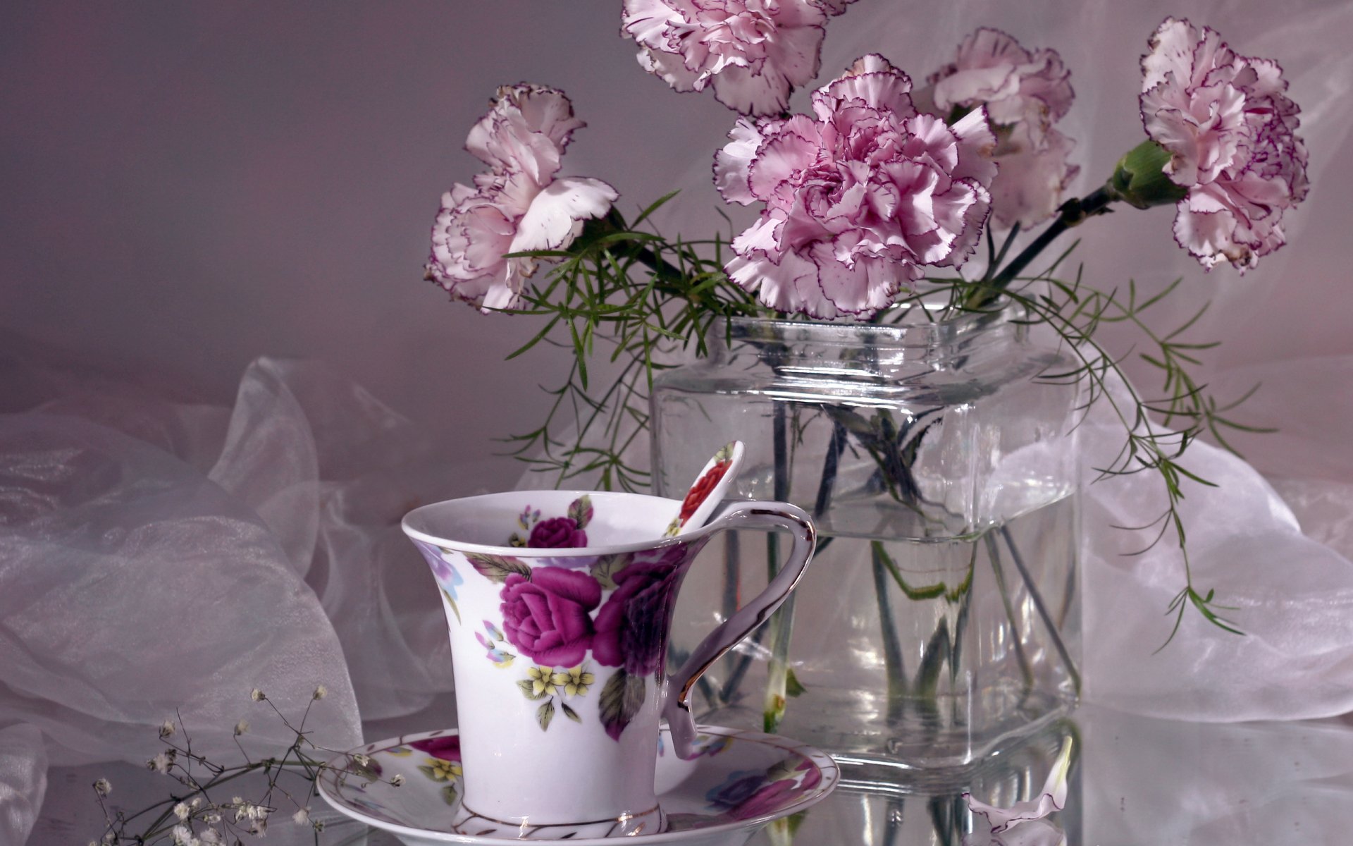 HD desktop wallpaper featuring a still life of pink carnations in a glass jar beside a floral-patterned cup and saucer, captured in delicate photography.