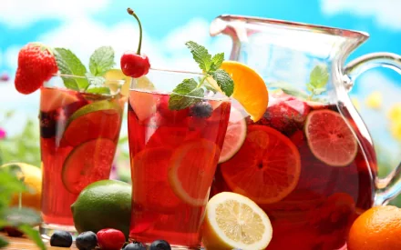 HD PC desktop wallpaper showing refreshing red fruit drink with berries, citrus slices, and mint leaves in glasses and a pitcher against a bright outdoor background.