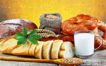 HD desktop wallpaper featuring various bread types, a glass of milk, and grains against a warm yellow background, highlighting wholesome food elements.