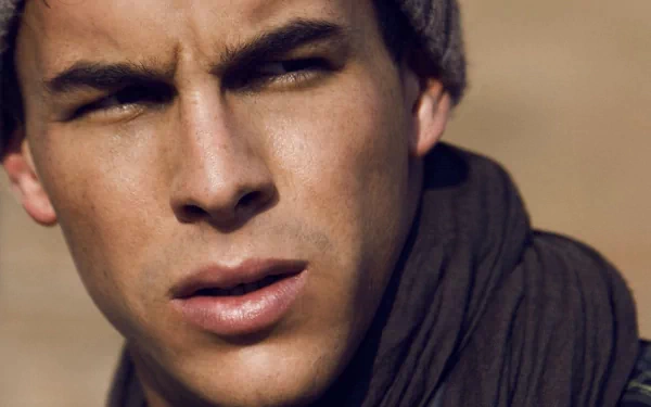 Close-up HD desktop wallpaper of celebrity Mario Casas wearing a beanie and scarf, with a warm-toned blurred background.