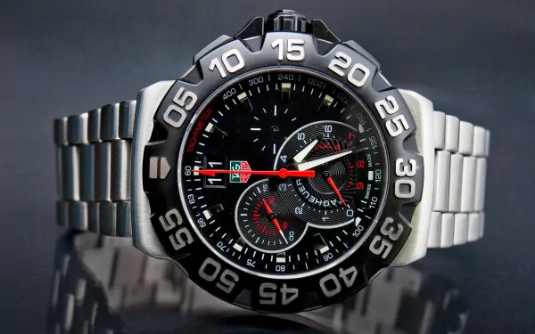 HD desktop wallpaper featuring a close-up of a man-made wristwatch with a detailed black dial and stainless steel band on a reflective surface.