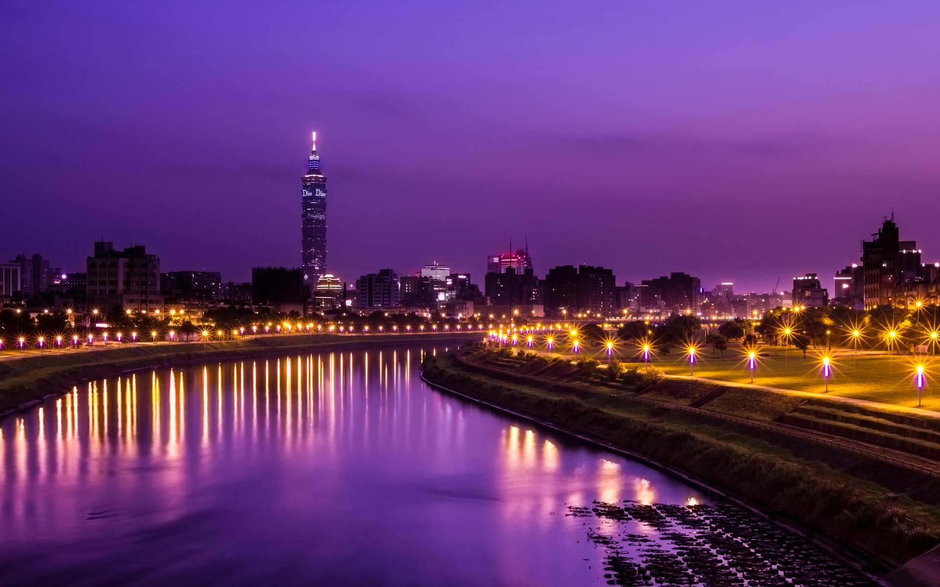 HD PC desktop wallpaper of Taipei's man-made skyline at dusk, Taipei 101 and city lights reflecting on a purple river with lit riverside road.