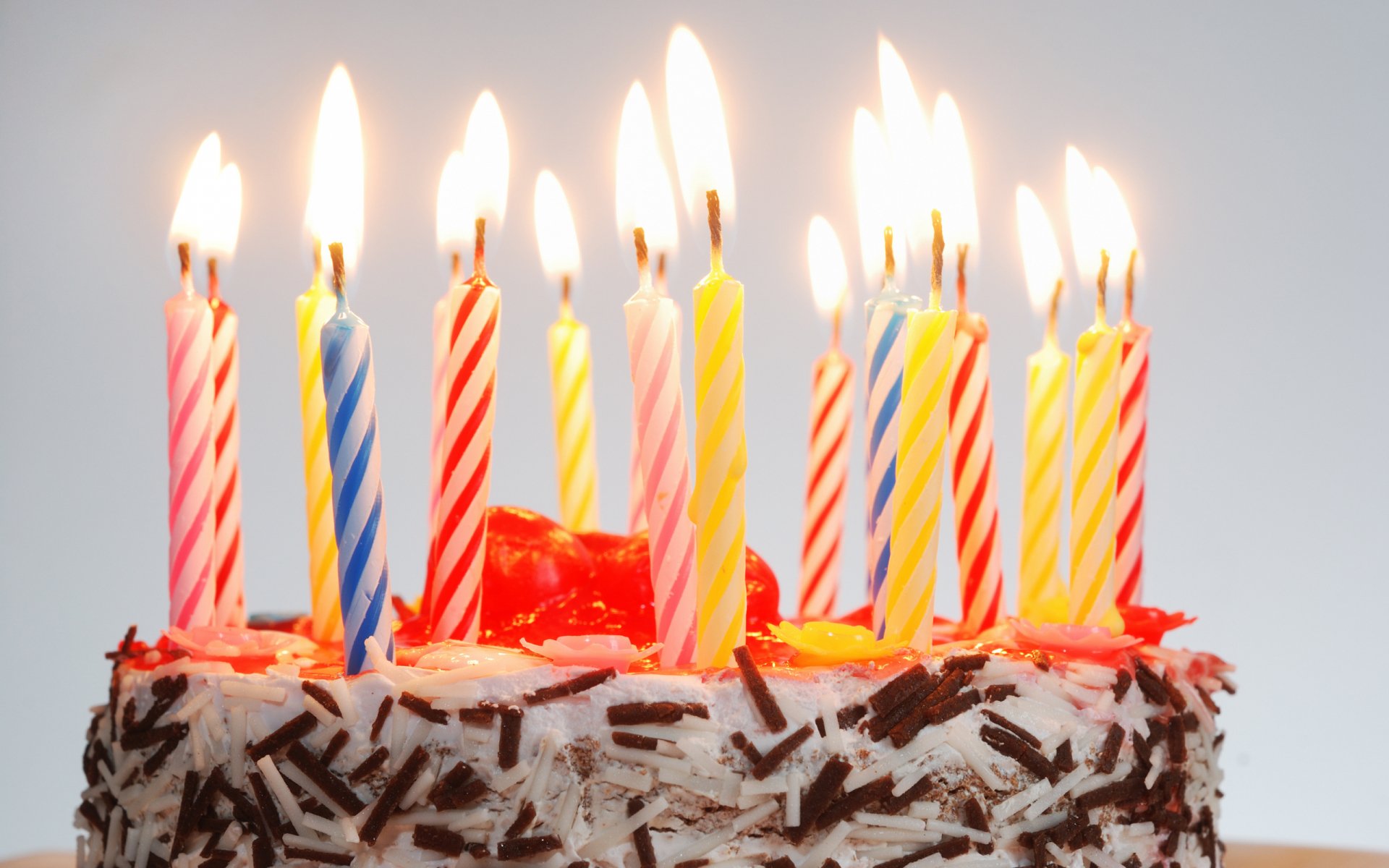 A colorful birthday cake adorned with lit candles, set against a light background, captures the festive spirit of celebration, making it an eye-catching HD desktop wallpaper.
