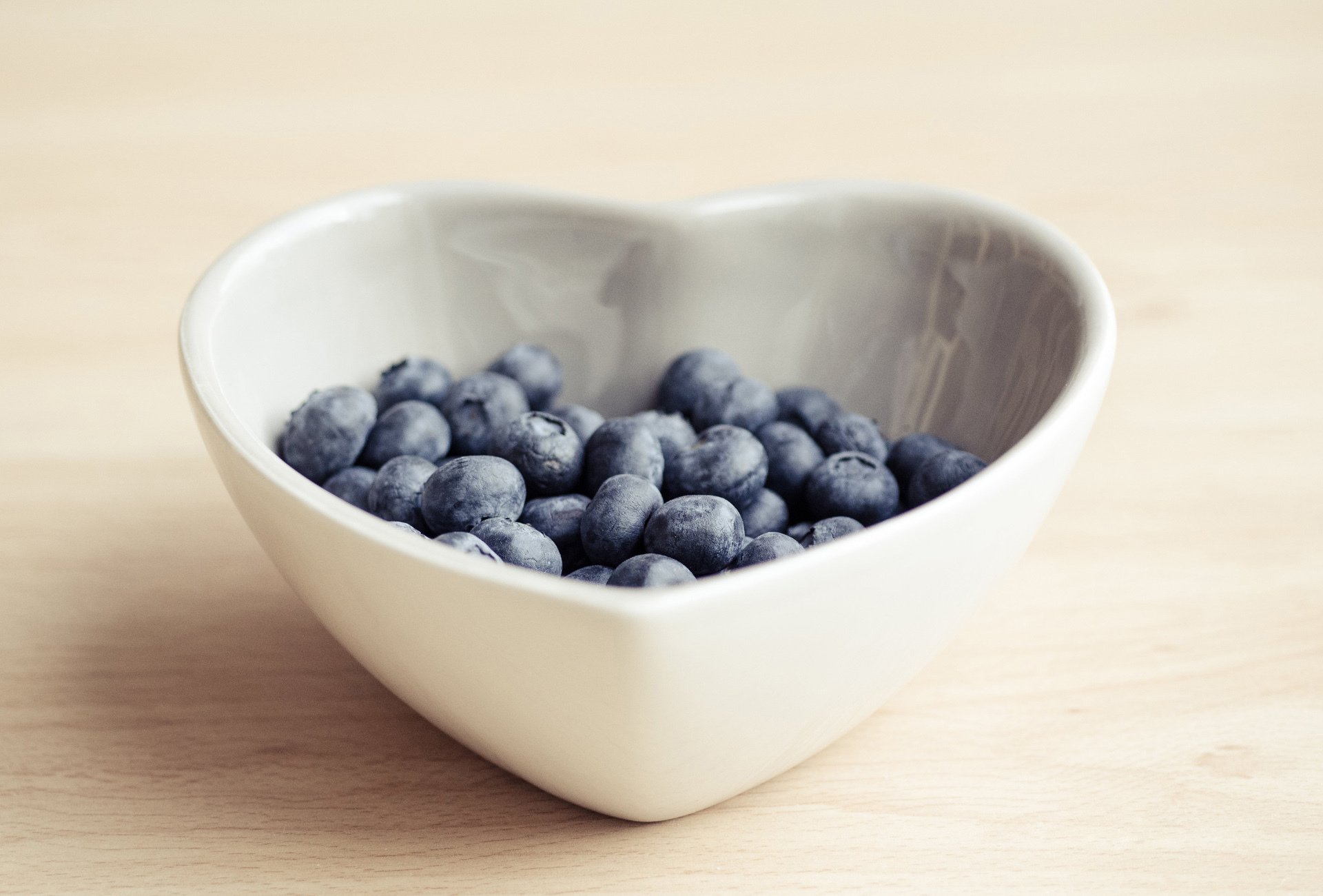 HD desktop wallpaper displaying fresh blueberries in a heart-shaped white bowl on a light wooden surface.