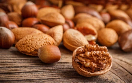 A close-up of various nuts, including almonds and walnuts, scattered on a rustic wooden surface, creating a warm and inviting food-themed desktop wallpaper.