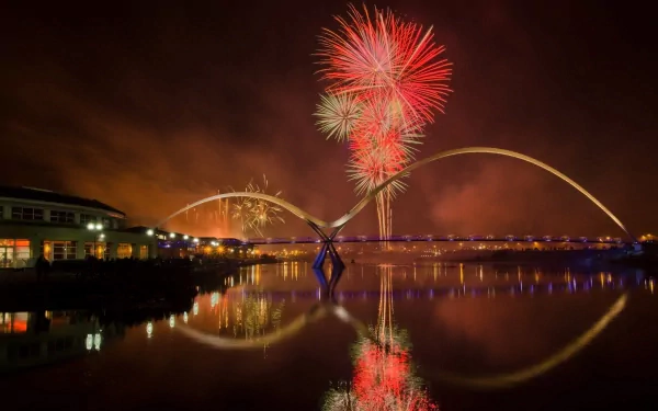 HD photography of vibrant red and gold fireworks bursting over a cityscape at night, reflected in calm water, designed as a PC desktop wallpaper and background.