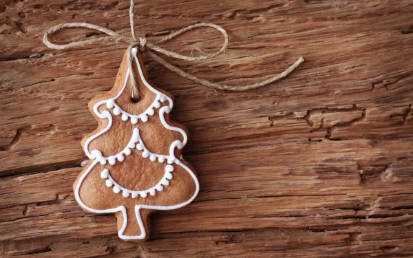 A gingerbread cookie shaped like a Christmas tree with white icing detail, hanging by a twine bow against a rustic wooden background, captured in 4K Ultra HD.