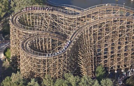 A wooden man-made roller coaster captured in an HD desktop wallpaper, showcasing intricate wooden tracks twisting above a forested area.