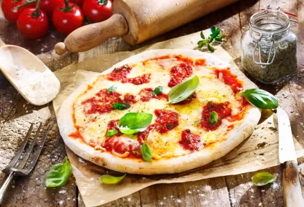 4K Ultra HD food wallpaper showing a freshly baked pizza topped with tomato sauce, cheese, and fresh basil on rustic parchment paper with kitchen tools in the background.