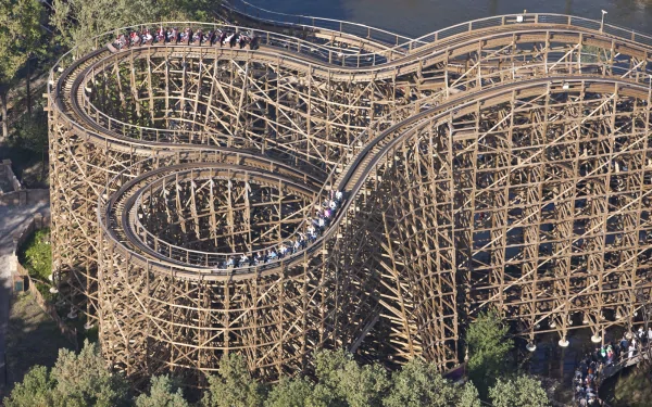 A wooden man-made roller coaster captured in an HD desktop wallpaper, showcasing intricate wooden tracks twisting above a forested area.