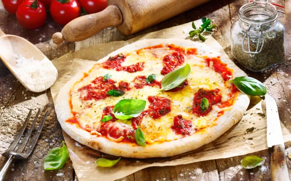 4K Ultra HD food wallpaper showing a freshly baked pizza topped with tomato sauce, cheese, and fresh basil on rustic parchment paper with kitchen tools in the background.