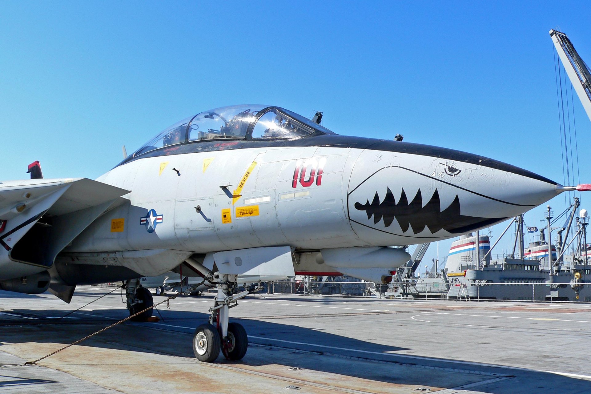 HD desktop wallpaper featuring a Grumman F-14 Tomcat military jet with shark mouth nose art on a clear day at an airbase.