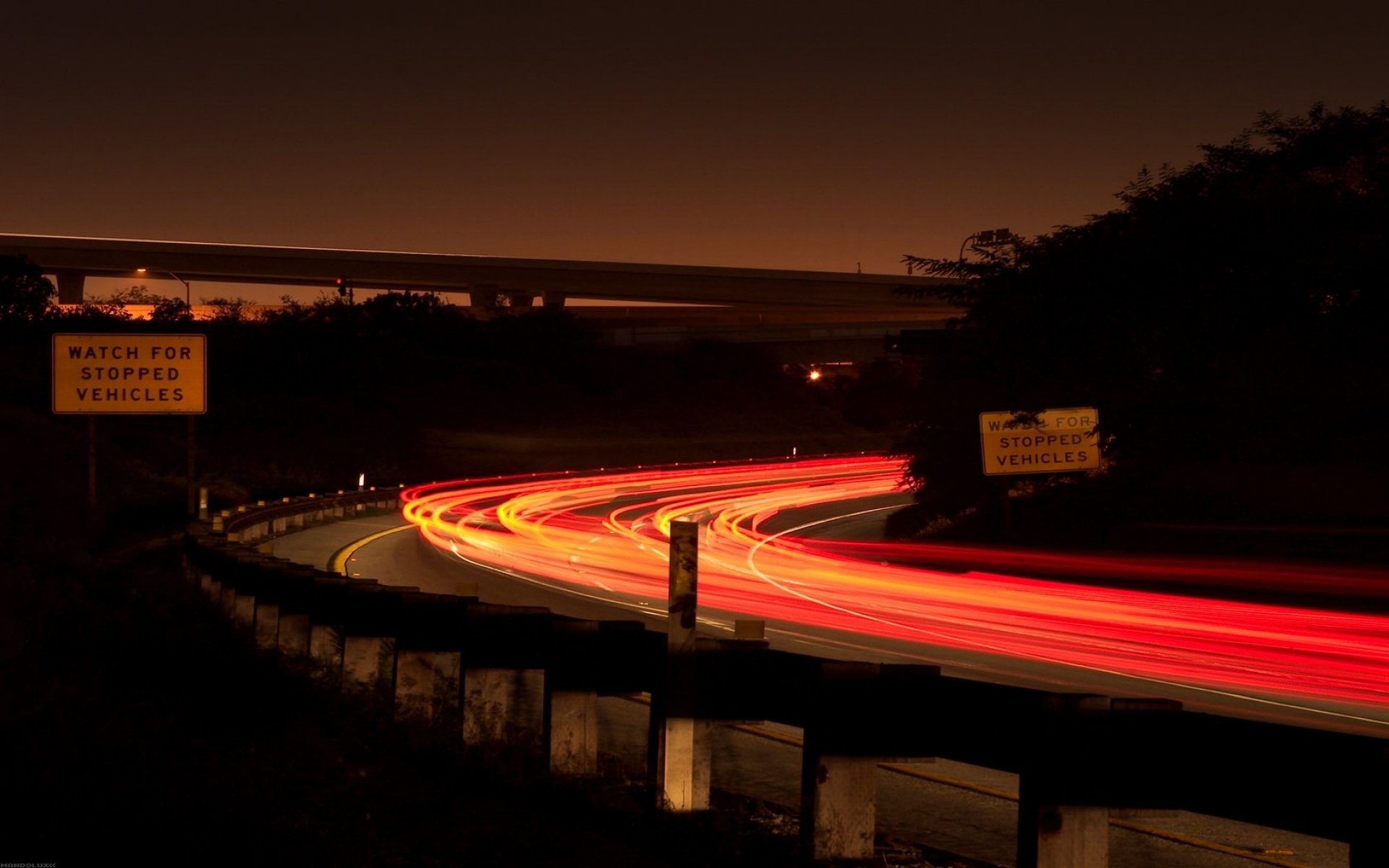 HD PC desktop wallpaper showcasing a time-lapse photograph of vibrant light trails curving along a highway at night.