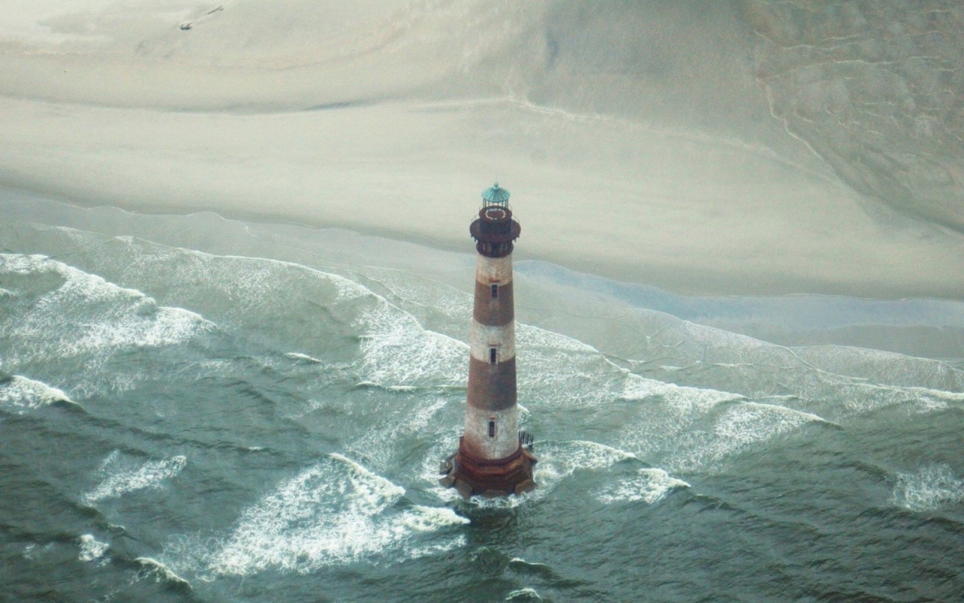 A man-made lighthouse stands tall in the ocean near a sandy shore, captured in HD for a striking PC desktop wallpaper and background.