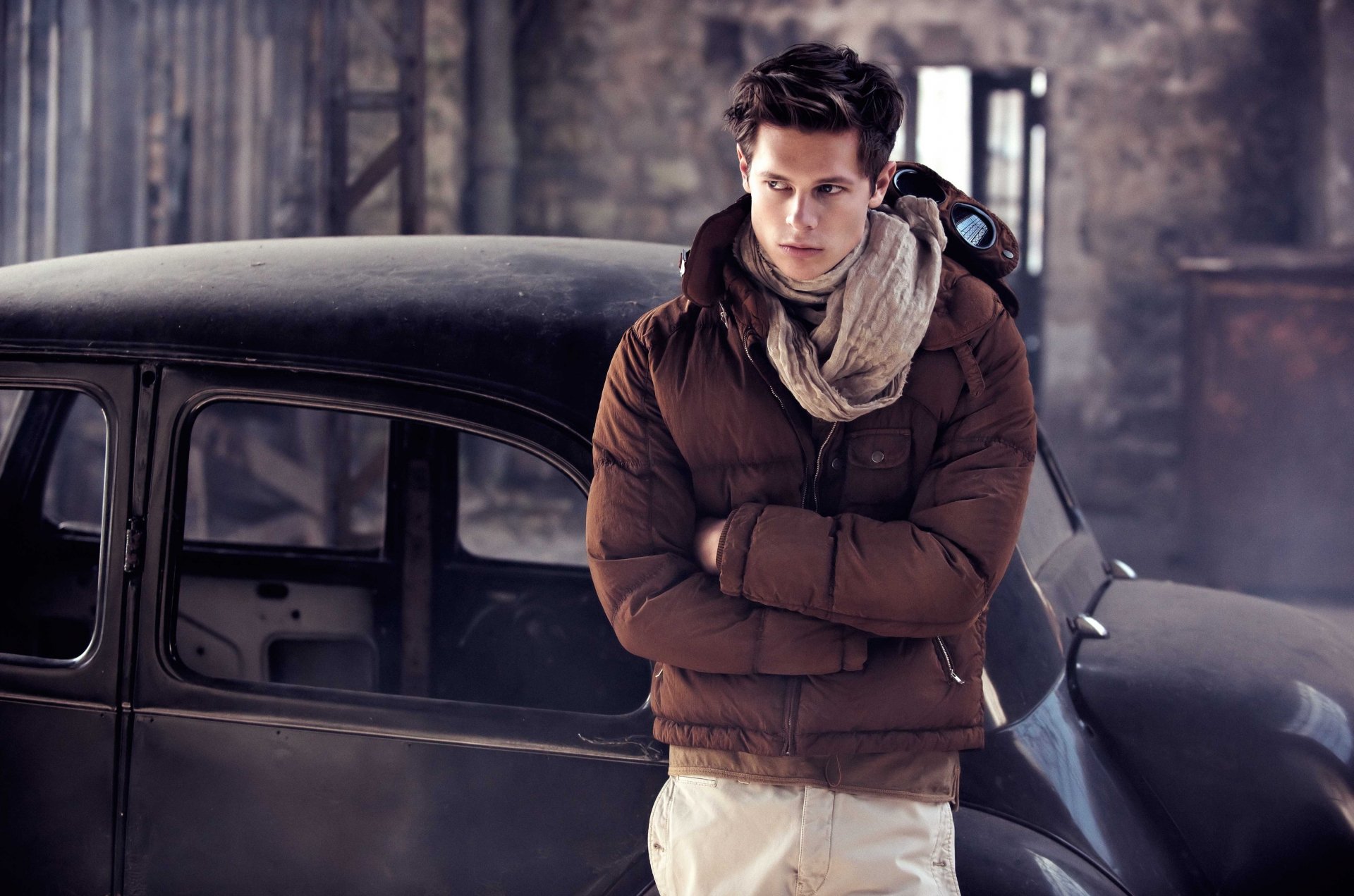 A man with brown hair and a scarf stands confidently in front of a classic car. The setting and the beautiful model create a striking HD desktop wallpaper background.