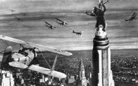 A dramatic scene from the 1933 movie King Kong, featuring the iconic giant ape atop the Empire State Building, surrounded by biplanes in an intense aerial confrontation.