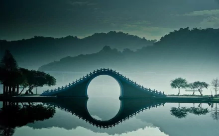 HD PC desktop wallpaper featuring a serene man-made Moon Bridge arching over calm water with misty hills and silhouetted trees in the background.