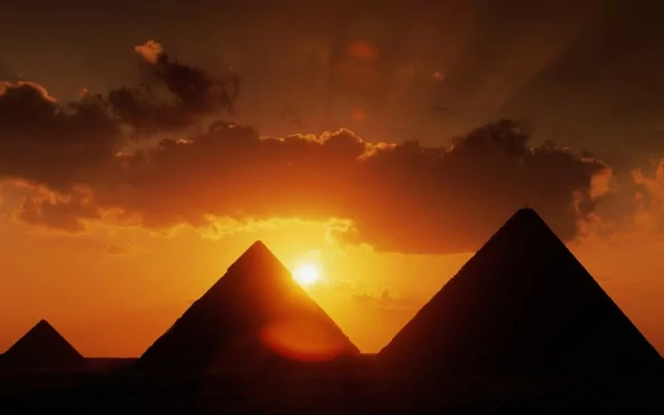 HD PC desktop wallpaper/background: man-made pyramids silhouetted against a fiery sunset, sun breaking through clouds and casting an orange glow across the sky.