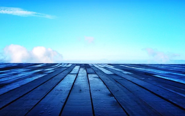 Artistic HD desktop wallpaper featuring a wooden planked surface with a vivid blue sky and wispy clouds in the background.