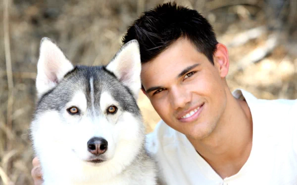 Taylor Lautner smiles warmly next to a Siberian Husky, set against a natural background, creating an inviting HD desktop wallpaper and background.