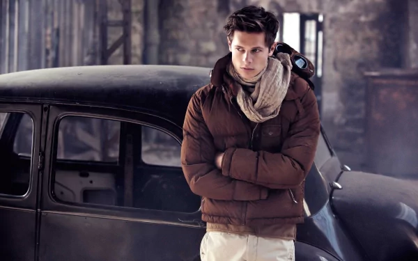 A man with brown hair and a scarf stands confidently in front of a classic car. The setting and the beautiful model create a striking HD desktop wallpaper background.