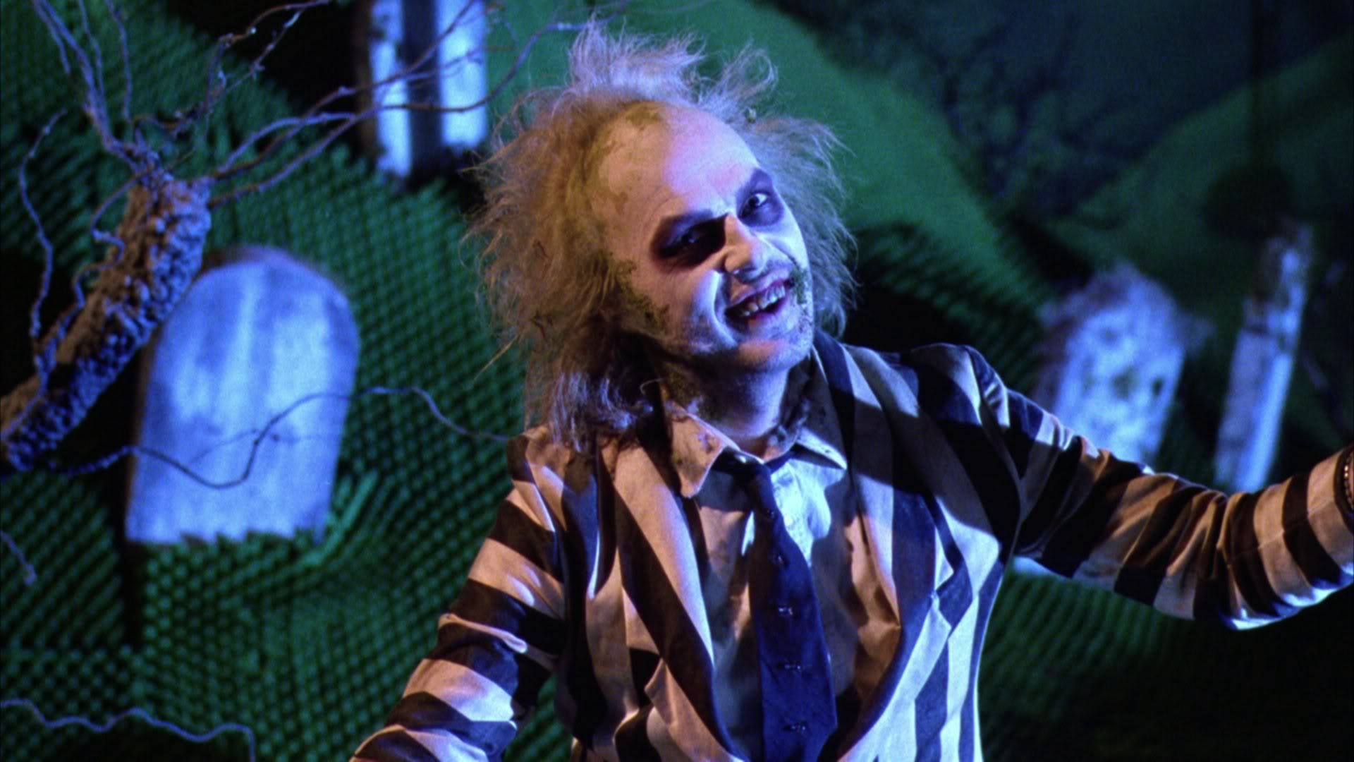 HD PC desktop wallpaper featuring Michael Keaton as Beetlejuice in his iconic black-and-white striped suit against a dark, eerie graveyard background.