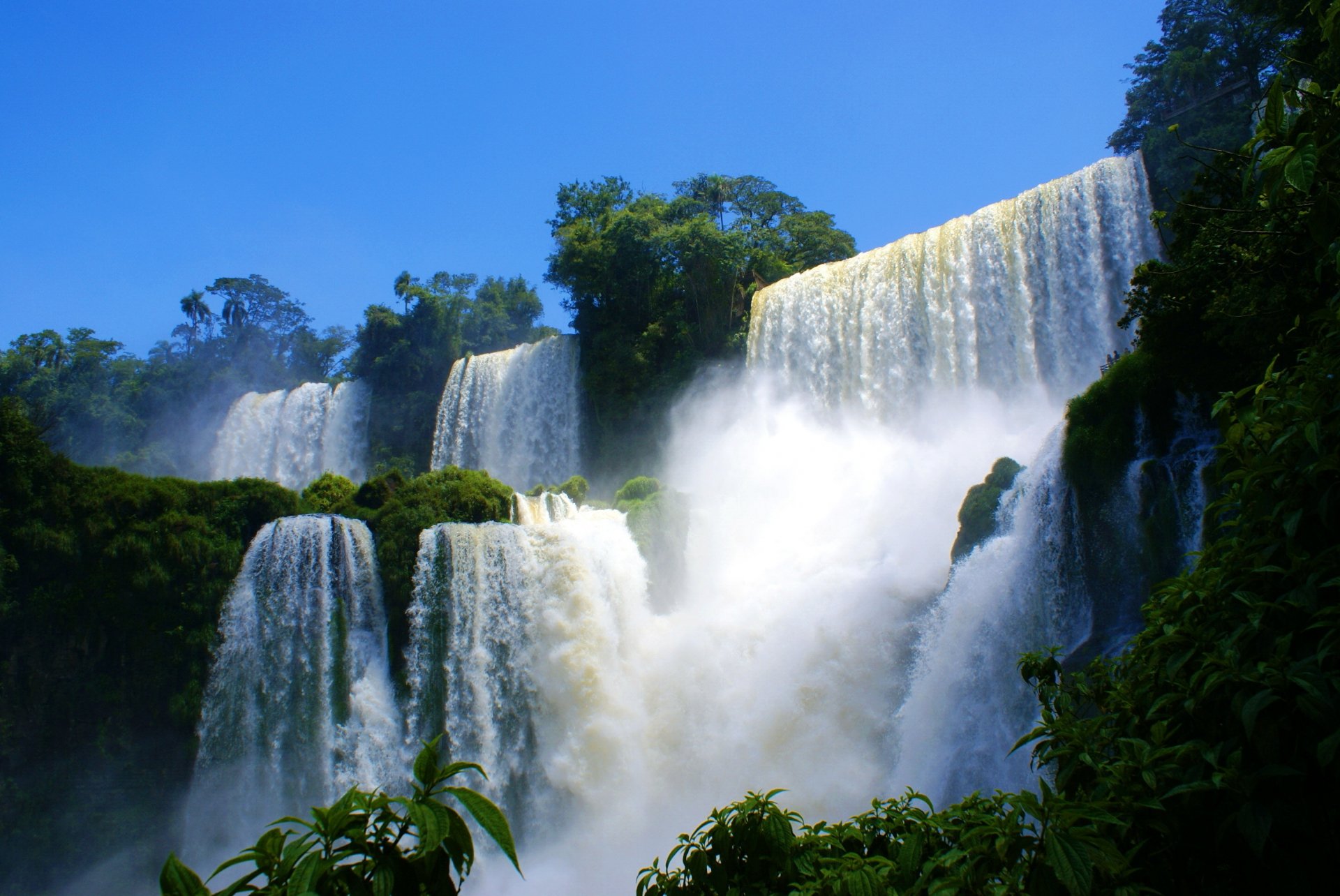 HD PC desktop wallpaper featuring a stunning nature scene with multiple cascading waterfalls surrounded by lush greenery under a clear blue sky.