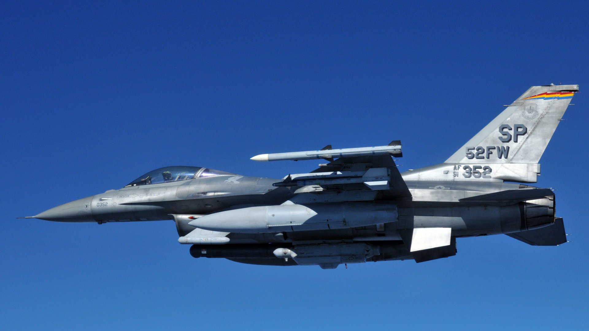 A General Dynamics F-16 Fighting Falcon jet fighter soars against a clear blue sky, showcasing its sleek design and military prowess. High-definition wallpaper for aviation enthusiasts.