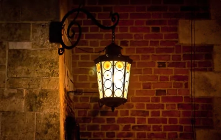 HD desktop wallpaper showing a man-made lamp post with warm light mounted on a textured brick and stone wall at night.