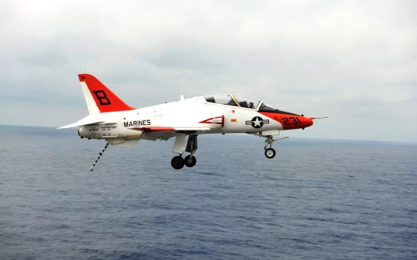 McDonnell Douglas T-45 Goshawk military aircraft with Marines markings flying over the ocean, captured in a clear sky HD desktop wallpaper background.