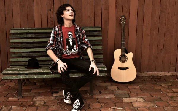 A young man sits on a weathered bench next to an acoustic guitar against a wooden fence, captured in a 4K Ultra HD PC desktop wallpaper.