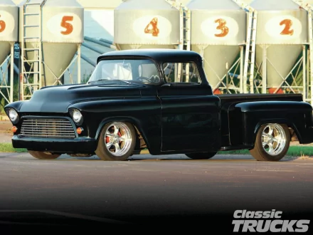 HD PC desktop wallpaper featuring a sleek black 1957 Chevrolet Stepside truck parked in front of industrial silos.