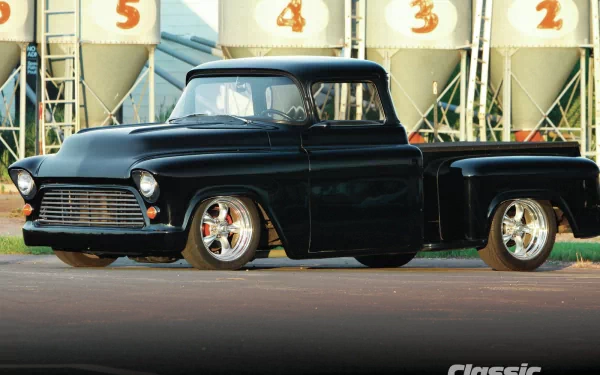 HD PC desktop wallpaper featuring a sleek black 1957 Chevrolet Stepside truck parked in front of industrial silos.