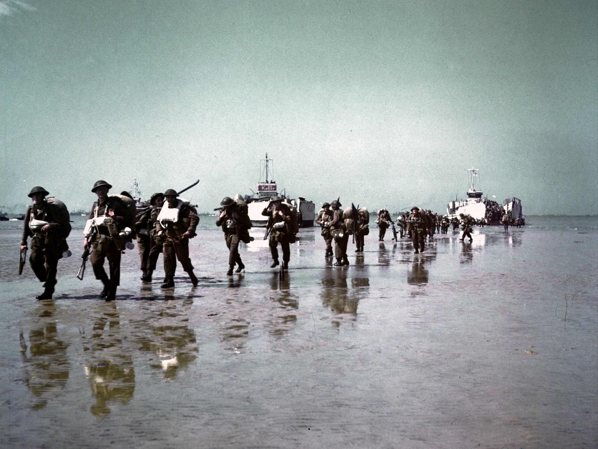World War II military scene: soldiers wading ashore from landing craft across a wet beach — HD PC desktop wallpaper/background.