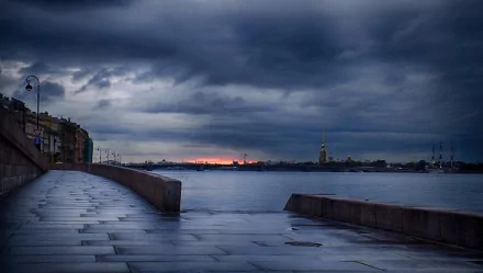 HD desktop wallpaper of a man-made waterfront promenade overlooking a town under a moody, cloudy sky at dusk.