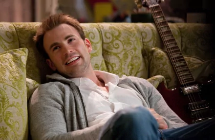 Chris Evans casually lounging on a green patterned sofa with a guitar in the background, captured in a vibrant HD wallpaper.