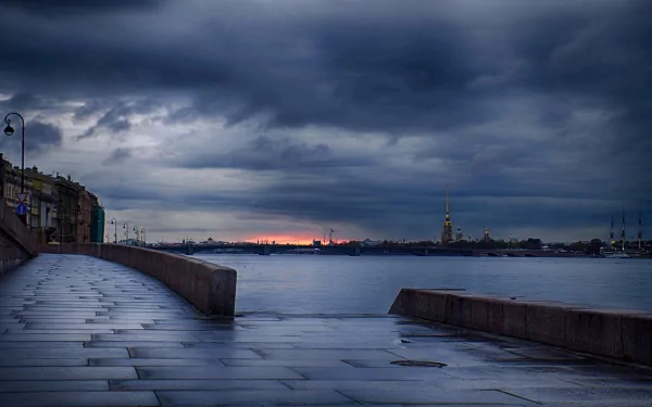 HD desktop wallpaper of a man-made waterfront promenade overlooking a town under a moody, cloudy sky at dusk.