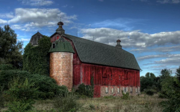 A vibrant red barn stands amidst lush greenery under a dramatic sky, showcasing a stunning man-made farm landscape. This HD image serves as an impressive desktop wallpaper.