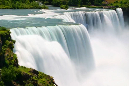 HD desktop wallpaper and background featuring the majestic Niagara Falls, showcasing cascading water surrounded by lush greenery. A breathtaking depiction of nature's beauty.