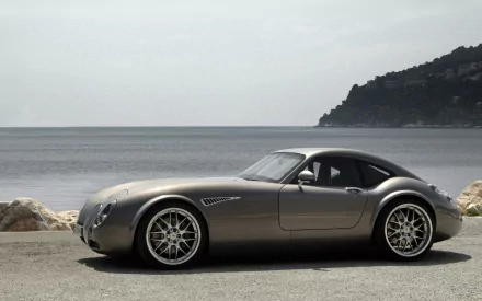 HD PC desktop wallpaper featuring a sleek Wiesmann GT MF4 vehicle parked by the seaside with a mountainous coastline in the background.