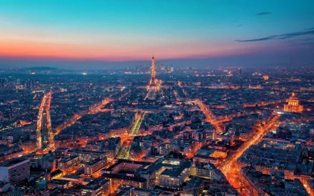 A stunning aerial view of Paris at dusk, showcasing the illuminated streets and iconic landmarks, including the Eiffel Tower, in vibrant hues of blue and orange. Man-made beauty shines in France.