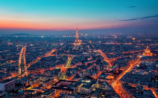 A stunning aerial view of Paris at dusk, showcasing the illuminated streets and iconic landmarks, including the Eiffel Tower, in vibrant hues of blue and orange. Man-made beauty shines in France.