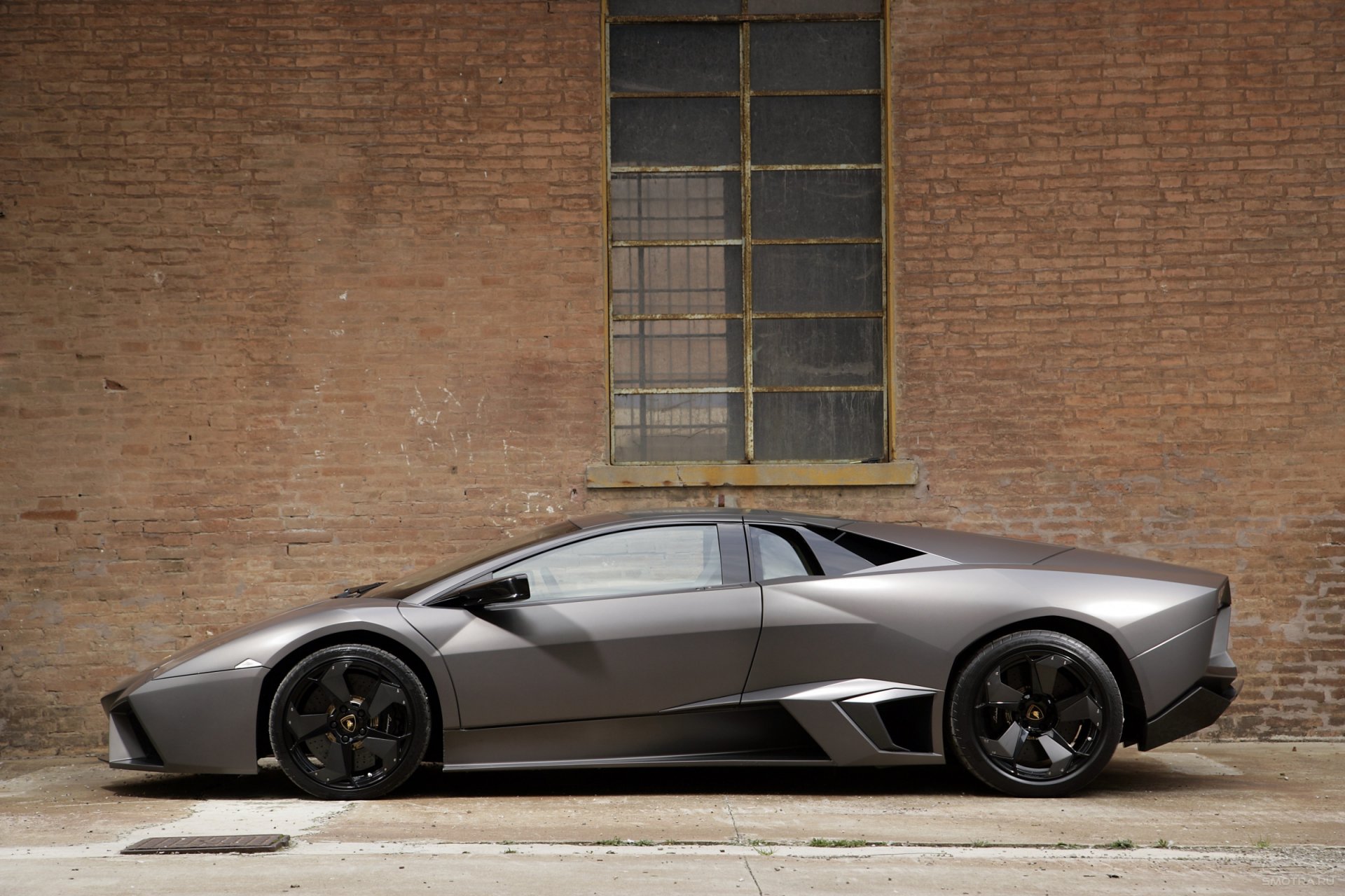 Silver Lamborghini Reventon supercar parked beside a brick wall, captured in a sharp HD desktop wallpaper showcasing the sleek design of this luxury vehicle.