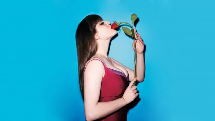 Kat Dennings poses gracefully with a rose against a vibrant blue background, captured in this HD desktop wallpaper. The image showcases her playful and artistic side.